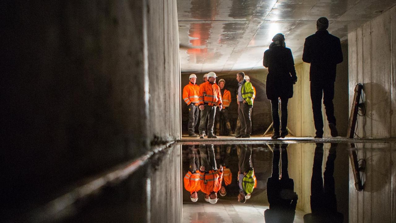 In einem Abwasserkanal in Berlin stehen mehrere Menschen deutlich entfernt vom Fotografen. Sie tragen zum Teil orange oder neongelbe Warnwesten. In einem Abwasserkanal in Berlin stehen mehrere Menschen deutlich entfernt vom Fotografen. Sie tragen zum Teil orange oder neongelbe Warnwesten.