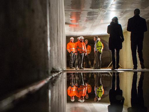 In einem Abwasserkanal in Berlin stehen mehrere Menschen deutlich entfernt vom Fotografen. Sie tragen zum Teil orange oder neongelbe Warnwesten.