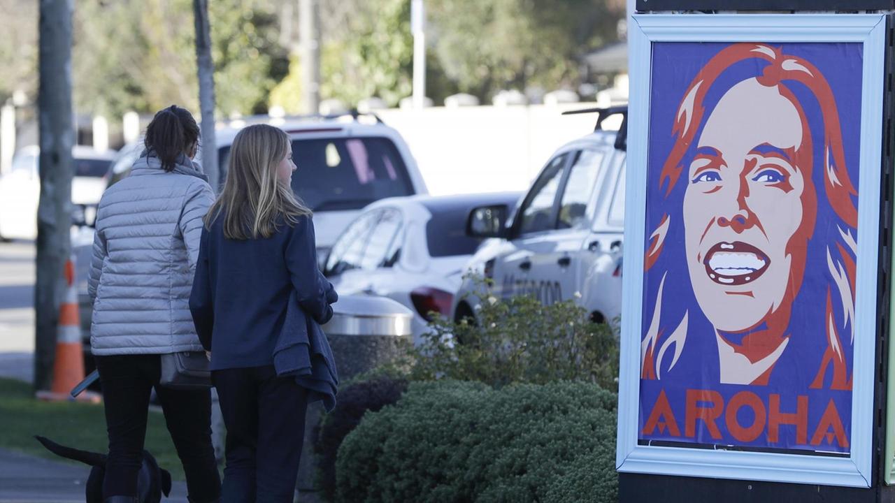 Straßenszene in Christchurch, Neuseeland: Zwei Fußgängerinnen und ein Hund passieren ein Plakat, dass die Premierministerin Jacinda Ardern mit dem Wort Aroha als Pop-Art-Illustration zeigt. Aroha bedeutet Liebe.