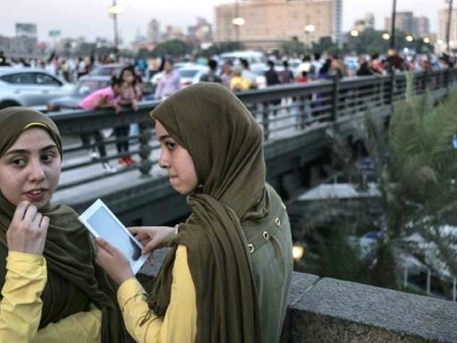 Zwei junge Frauen auf einer Brücke in Kairo. Eine trägt ein Handy. Beide tragen Kopftuch.