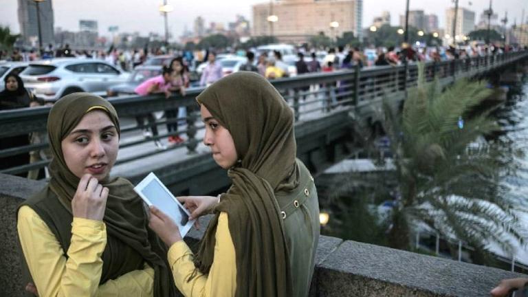 Zwei junge Frauen auf einer Brücke in Kairo. Eine trägt ein Handy. Beide tragen Kopftuch.