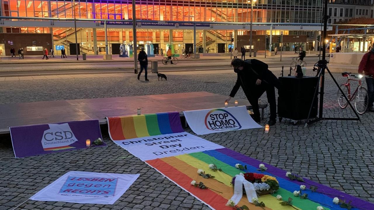 Eine Regenbogenfahne, ein Kranz und weiße Blumen erinnern auf dem Altmarkt vor dem Kulturpalast in Dresden an die Opfer einer Messerattacke Eine Regenbogenfahne, ein Kranz und weiße Blumen erinnern auf dem Altmarkt vor dem Kulturpalast in Dresden an die Opfer einer Messerattacke