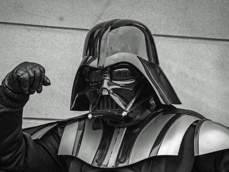 "I am your father" (Darth Vader, Star Wars). Ein Mann in voller Rüstung hebt den rechten Arm, die Hand zur Faust geballt und schaut böse in die Kamera.