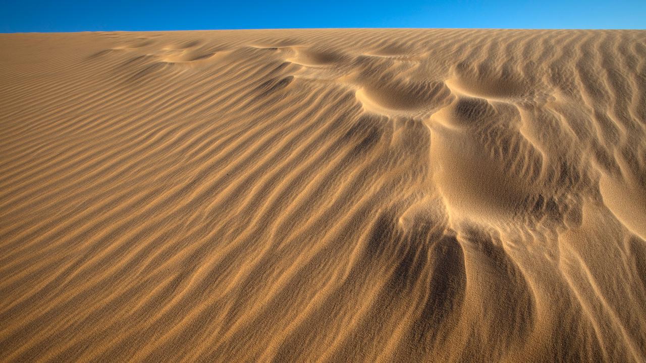 Verwehte Fußspuren auf einer Sanddüne bei Assuan in Ägypten, im Hintergrund blauer Himmel Verwehte Fußspuren auf einer Sanddüne bei Assuan in Ägypten, im Hintergrund blauer Himmel