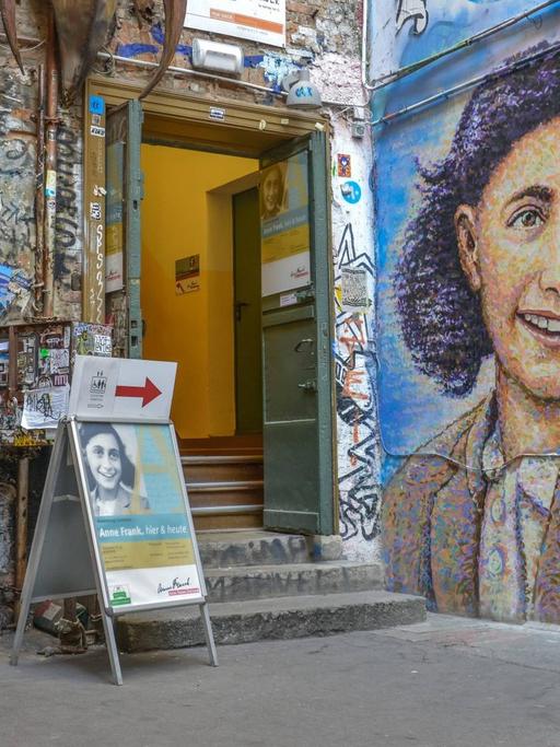 Ein junge Frau mit Stoffbeutel vor einem Graffiti, das Anne Frank zeigt, vor dem Anne Frank Zentrum im Hinterhof an der Rosenthaler Straße in Berlin-Mitte