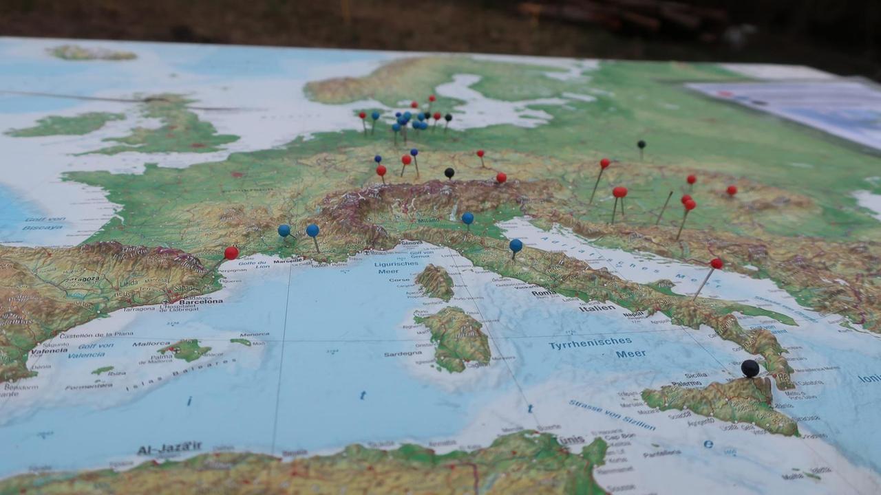 Eine Landkarte, auf der Stellen in verschiedenen Ländern mit Stecknadeln markiert sind Eine Landkarte, auf der Stellen in verschiedenen Ländern mit Stecknadeln markiert sind