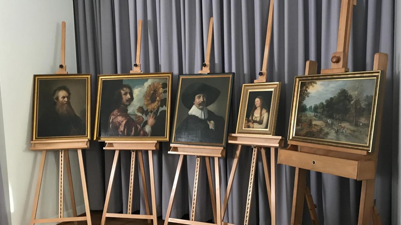 Vor einem grauen Vorhang stehen fünf Holzstaffeleien. In den Staffeleien werden die gestohlenen Gemälde aus Gotha präsentiert