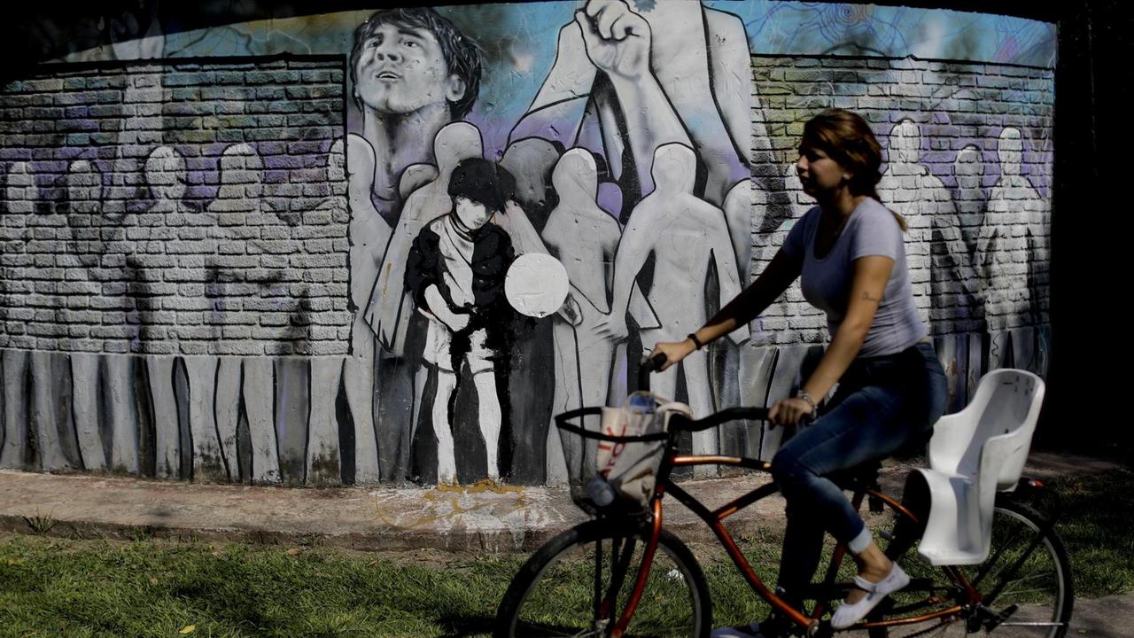 Eine Frau fährt mit dem Fahrrad an der Schule von Fussbalstar Lionel Messi in Rosario in Argentinien vorbei, auf deren Fassade ein Fussball-Mural gemalt wurde, aufgenommen im April 2018. Eine Frau fährt mit dem Fahrrad an der Schule von Fussbalstar Lionel Messi in Rosario in Argentinien vorbei, auf deren Fassade ein Fussball-Mural gemalt wurde, aufgenommen im April 2018.