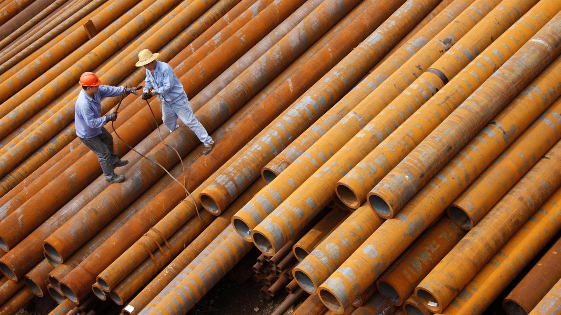 Chinesische Arbeiter in Huaibei bewegen sich auf rieigen Stahlrohren.
