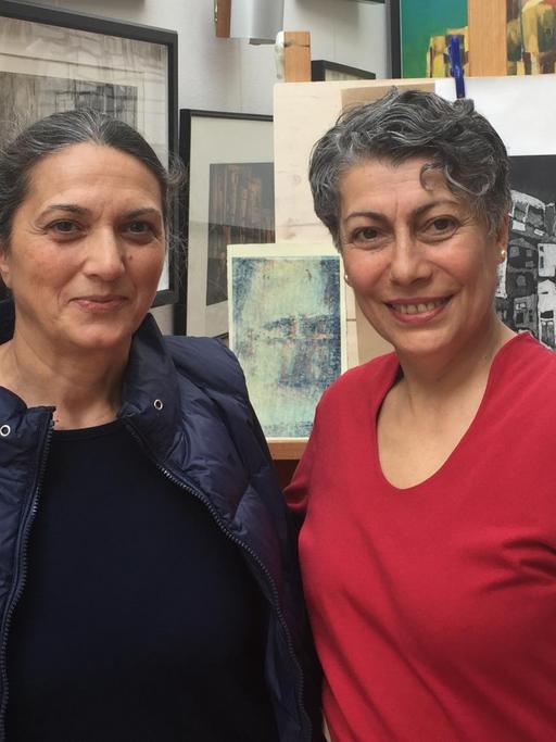 Tülay Seker und Sevim Celik-Lorenzen, zwei türkischstämmige Frauen, stehen in einem Raum vor einer Wand mit vielen Bildern.