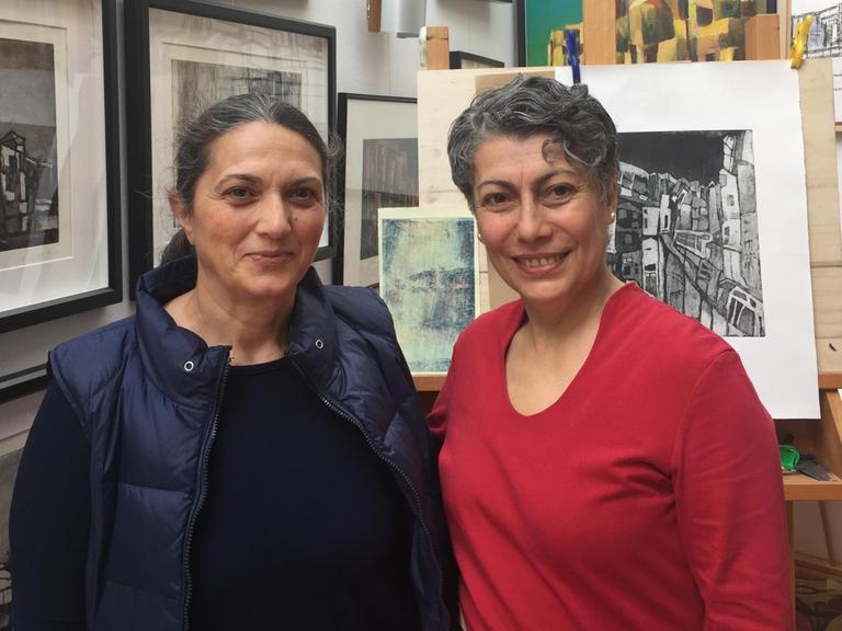 Tülay Seker und Sevim Celik-Lorenzen, zwei türkischstämmige Frauen, stehen in einem Raum vor einer Wand mit vielen Bildern.