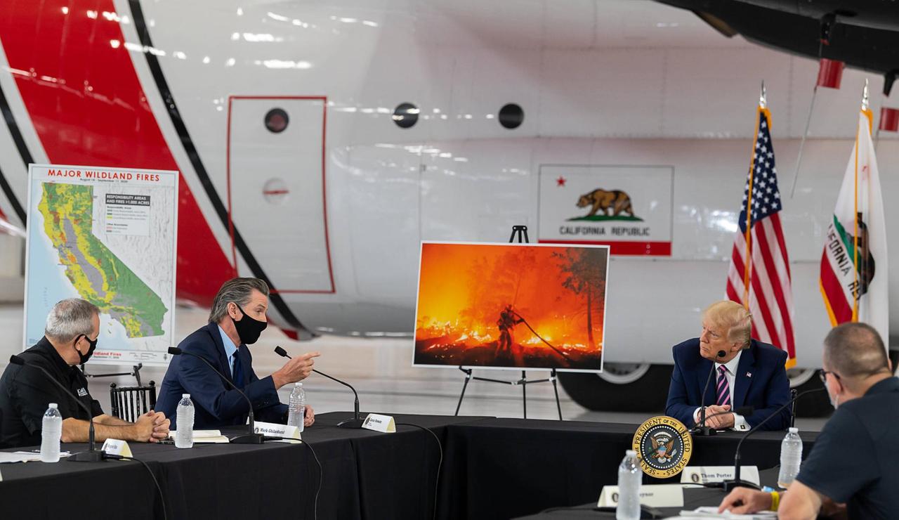 US-Präsident Donald Trump diskutiert die Brände mit dem Kalifornischen Gouverneur Gavin Newson. Zwischen den beiden steht ein Bild, dass die Brände zeigt.