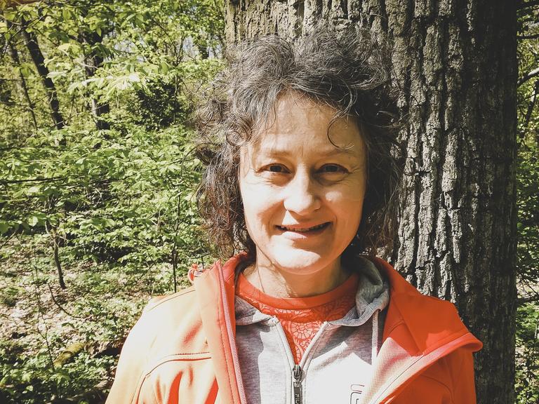 Private Aufnahme von Birgit Saalfrank. Sie steht in Funktionskleidung vor einem Baum inmitten eines Waldes.