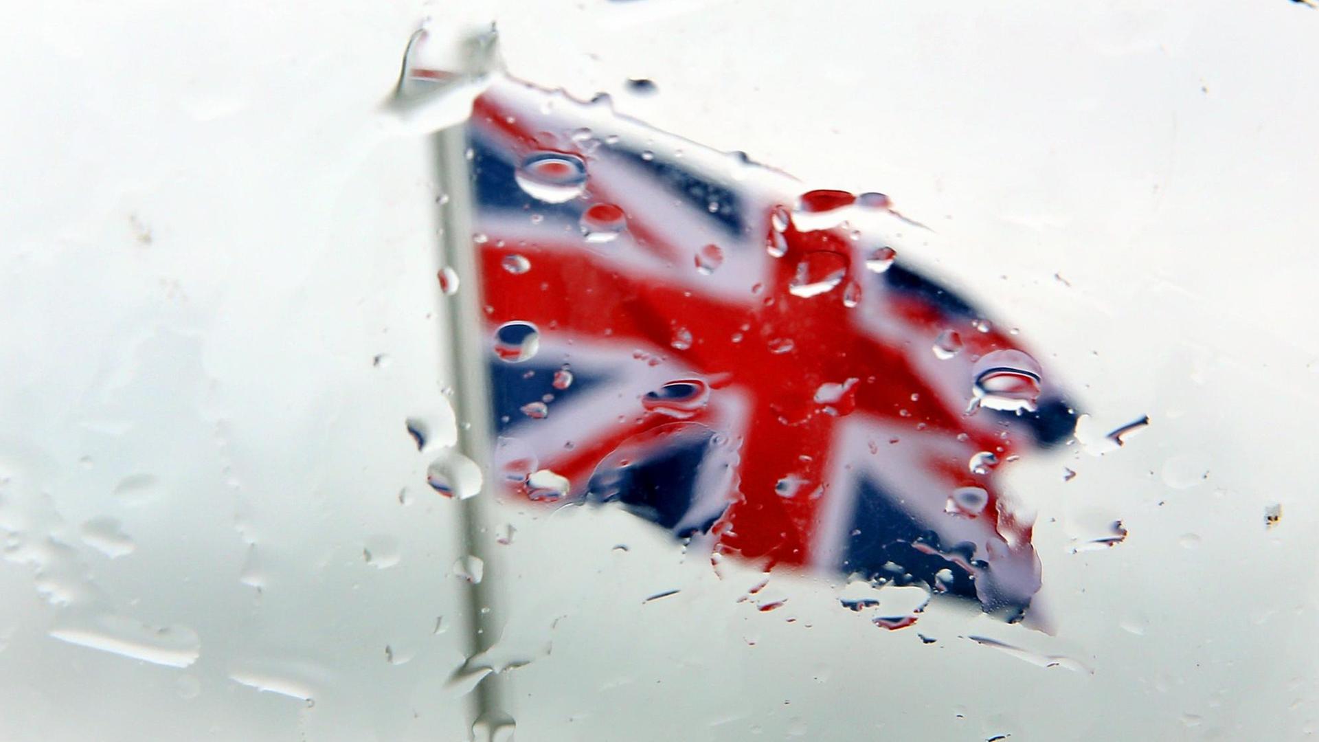 Blick durch eine vom Regen benetzte Autoscheibe auf eine britische Fahne.