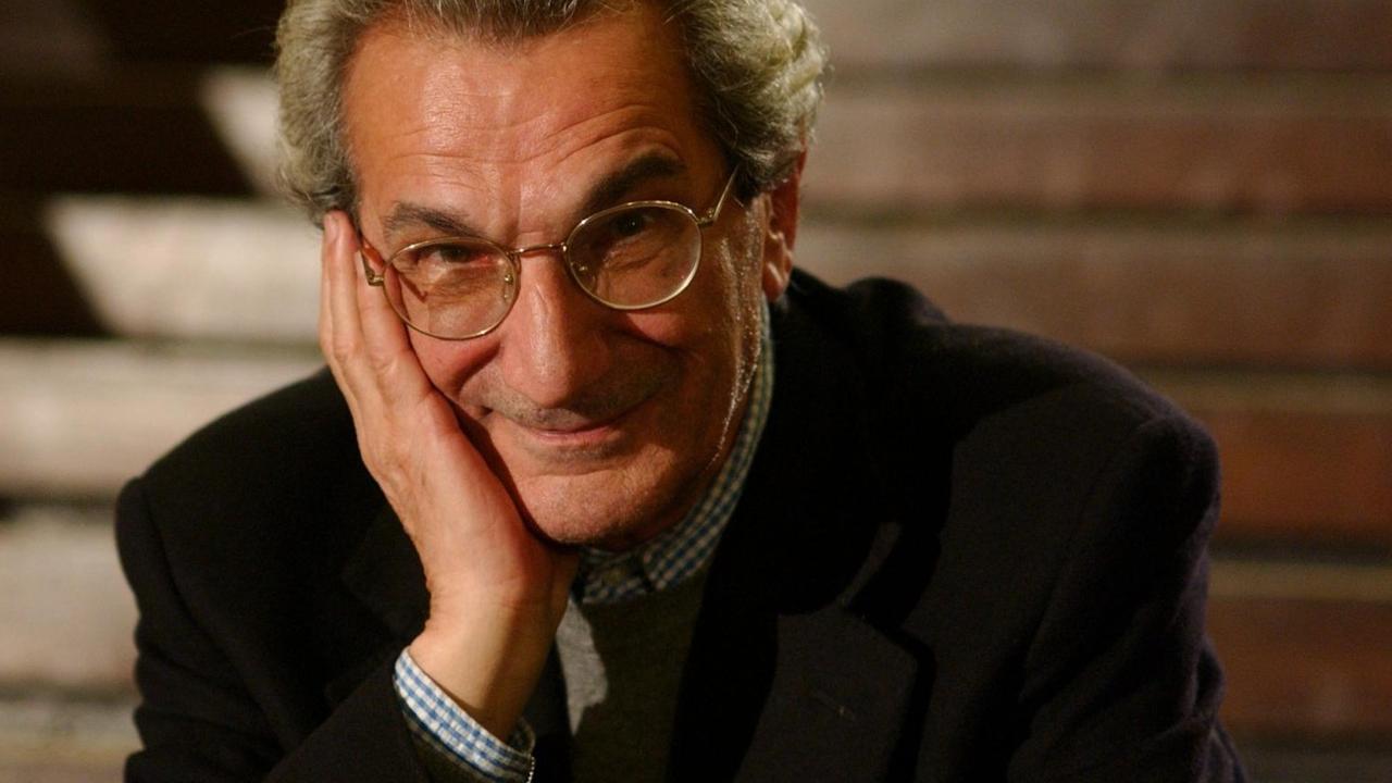 Antonio Negri, ein freundlicher älterer Herr, sitzt auf Treppenstufen, hat die Hand am Gesicht liegen und lächelt in die Kamera. Antonio Negri, ein freundlicher älterer Herr, sitzt auf Treppenstufen, hat die Hand am Gesicht liegen und lächelt in die Kamera.