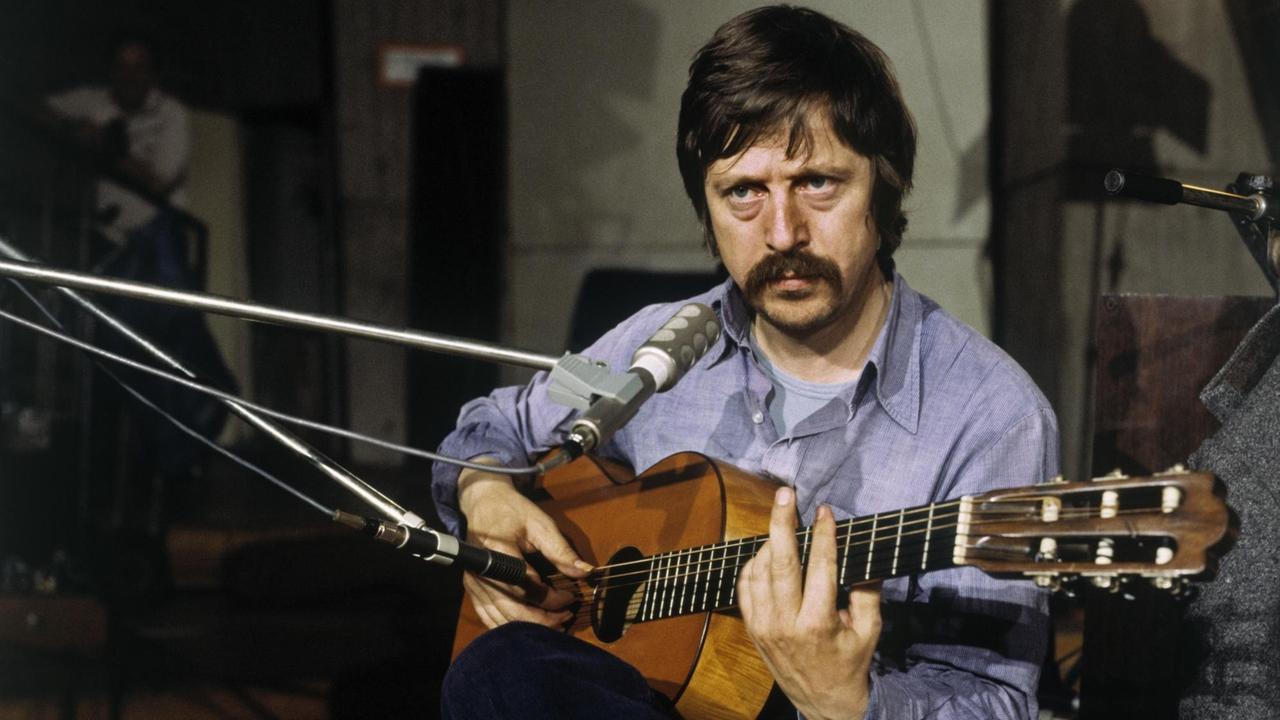 Wolf Biermann sitzt mit Gitarre vor einem Mikrofon. Wolf Biermann sitzt mit Gitarre vor einem Mikrofon.