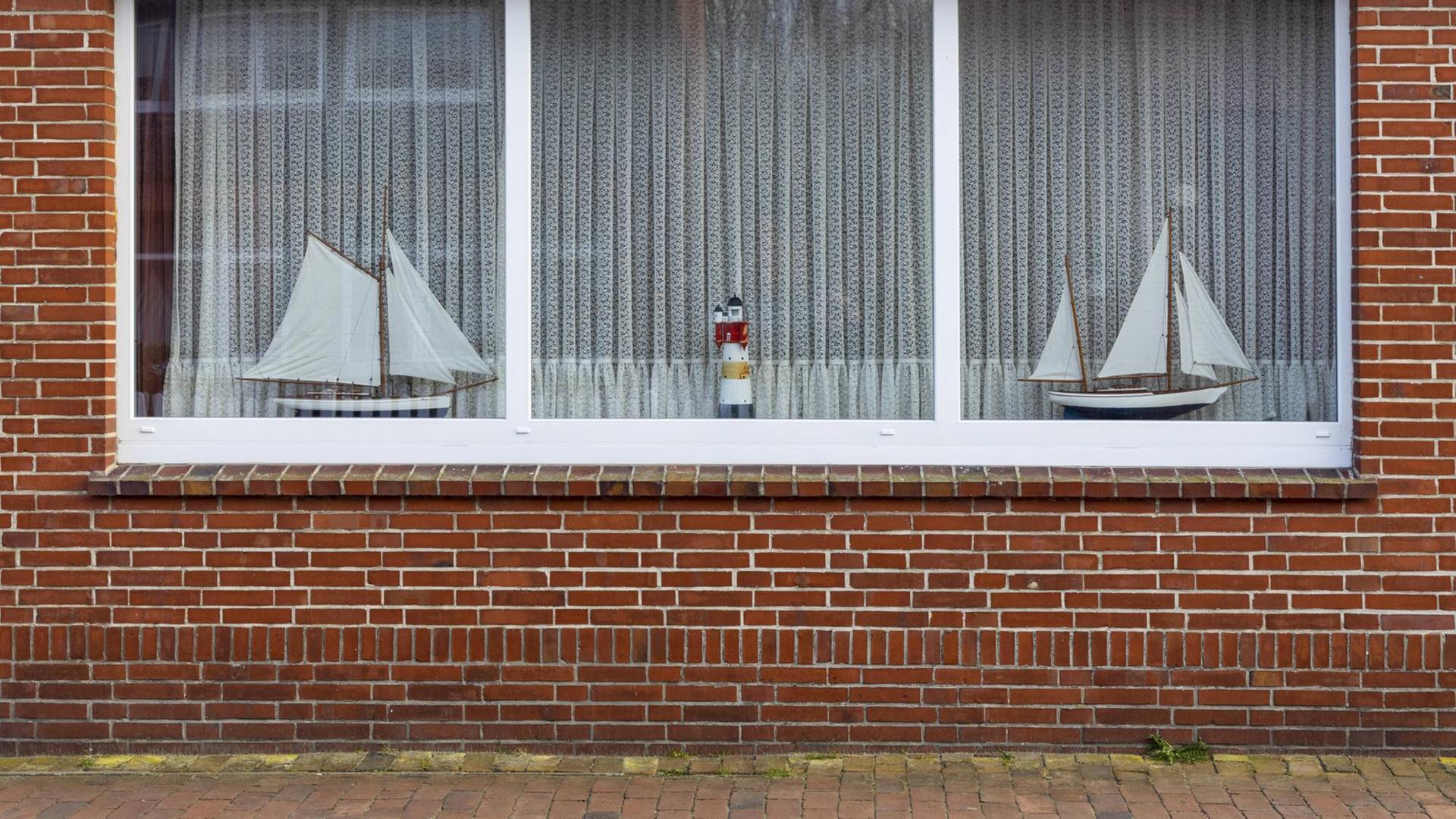 Fassade eines Backsteinhauses. Im Fenster steht ein Leuchtturm und zwei Segelboote, die Gardinen sind zugezogen. Fassade eines Backsteinhauses. Im Fenster steht ein Leuchtturm und zwei Segelboote, die Gardinen sind zugezogen.