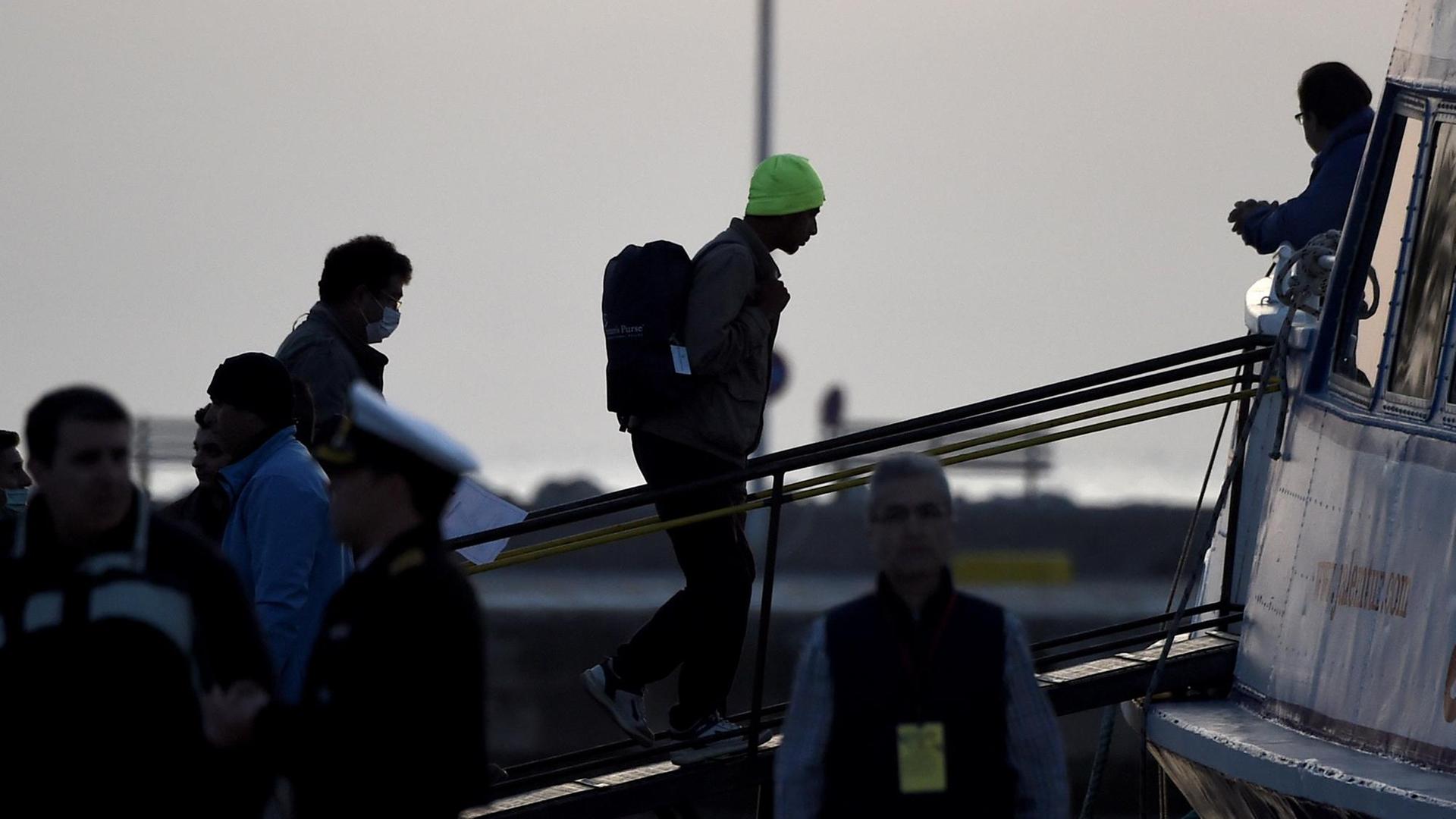 Sie sehen die Silhouetten von Flüchtingen, die auf der Insel Lesbos an Bord eines Schiffes gehen. Sie sehen die Silhouetten von Flüchtingen, die auf der Insel Lesbos an Bord eines Schiffes gehen.