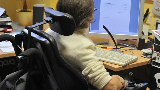 Eine Frau sitzt in ihrem Rollstuhl vor einem Computerarbeitsplatz.
