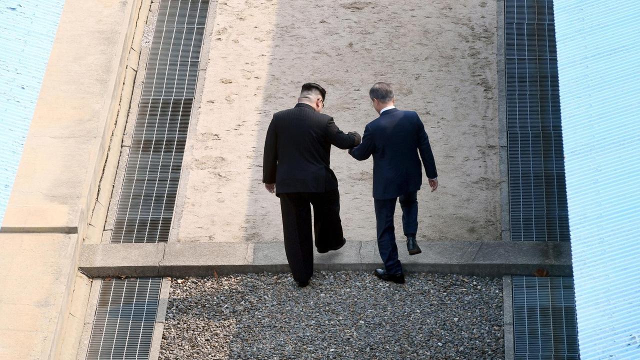 Eine Aufnahme zeigt wie der nordkoreanische Führer Kim Jong Un (L) die Hand des südkoreanischen Präsidenten Moon Jae-in (R) hält, während sie die militärische Demarkationslinie (MDL) überschreiten. Beide trafen sich beim interkoreanischen Gipfel am 27. April 2018 in Panmunjom, Südkorea.