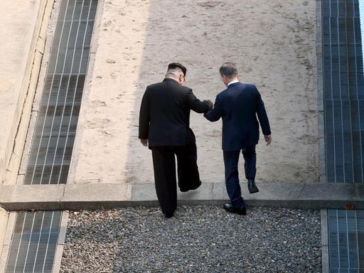 Eine Aufnahme zeigt wie der nordkoreanische Führer Kim Jong Un (L) die Hand des südkoreanischen Präsidenten Moon Jae-in (R) hält, während sie die militärische Demarkationslinie (MDL) überschreiten. Beide trafen sich beim interkoreanischen Gipfel am 27. April 2018 in Panmunjom, Südkorea.