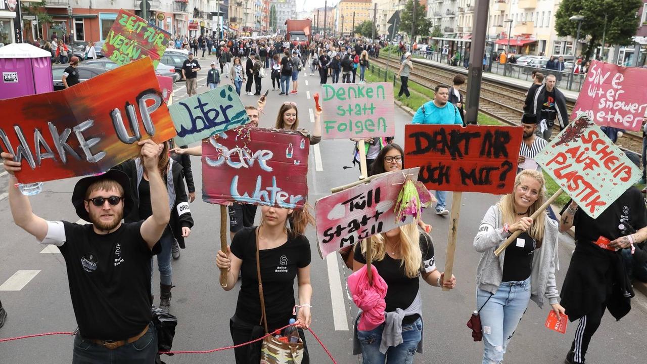 Junge Menschen demonstrieren in Berlin. Sie tragen Schilder mit der Aufschrift: WAKE UP - ZEIT FÜR VERÄNDERUNG! - Water Save Water - Denken statt folgen - Tüll statt Müll - SCHEIß AUF PLASTIK