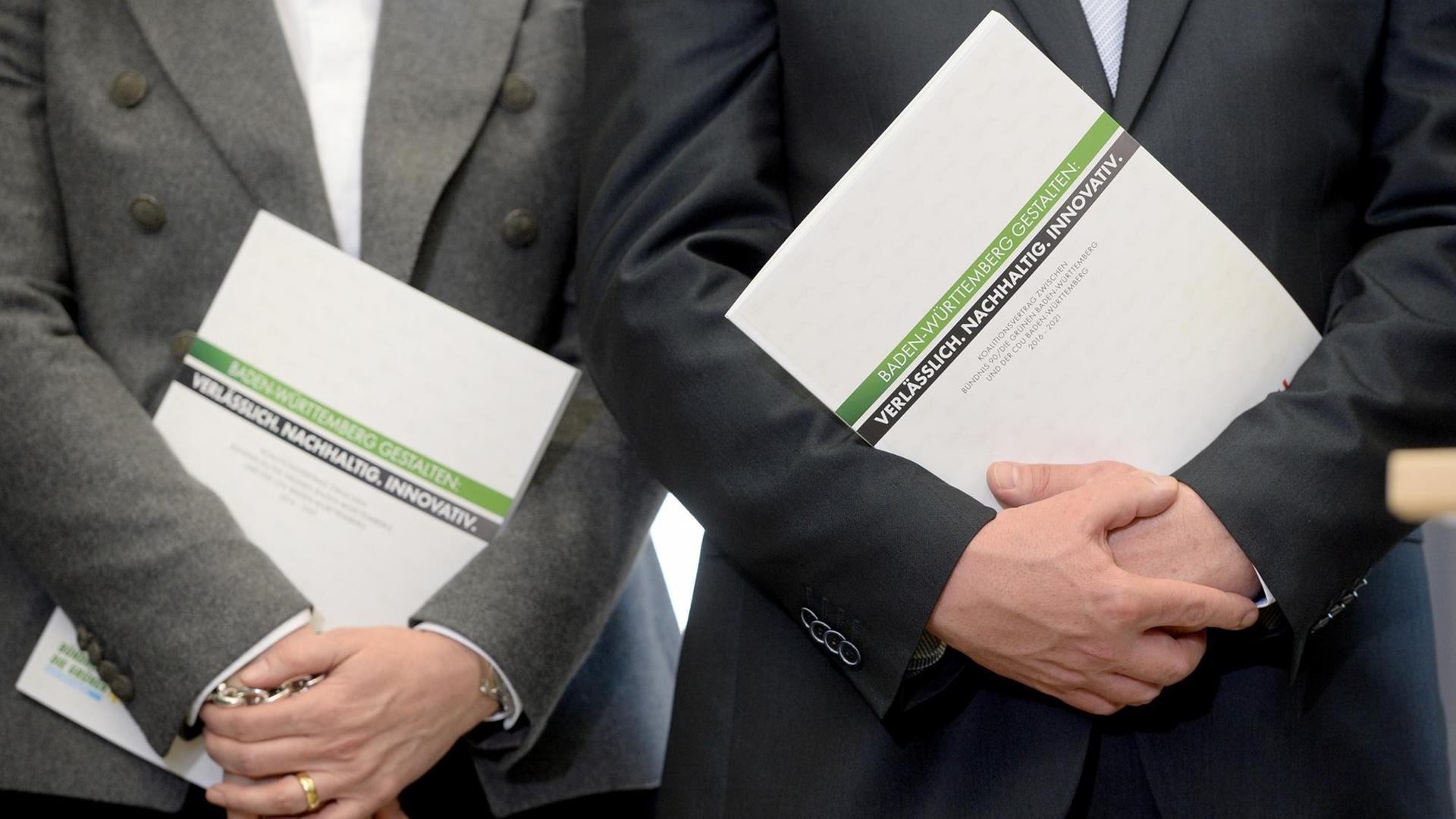 Zwei Männer in Anzügen halten den ersten grün-schwarzen Koalitionsvertrag einer deutschen Landesregierung in ihren Händen. Zwei Männer in Anzügen halten den ersten grün-schwarzen Koalitionsvertrag einer deutschen Landesregierung in ihren Händen.