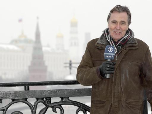 Hermann Krause steht mit einem Mikrofon der ARD vor einer verschneiten Winderlandschaft in Moskau.