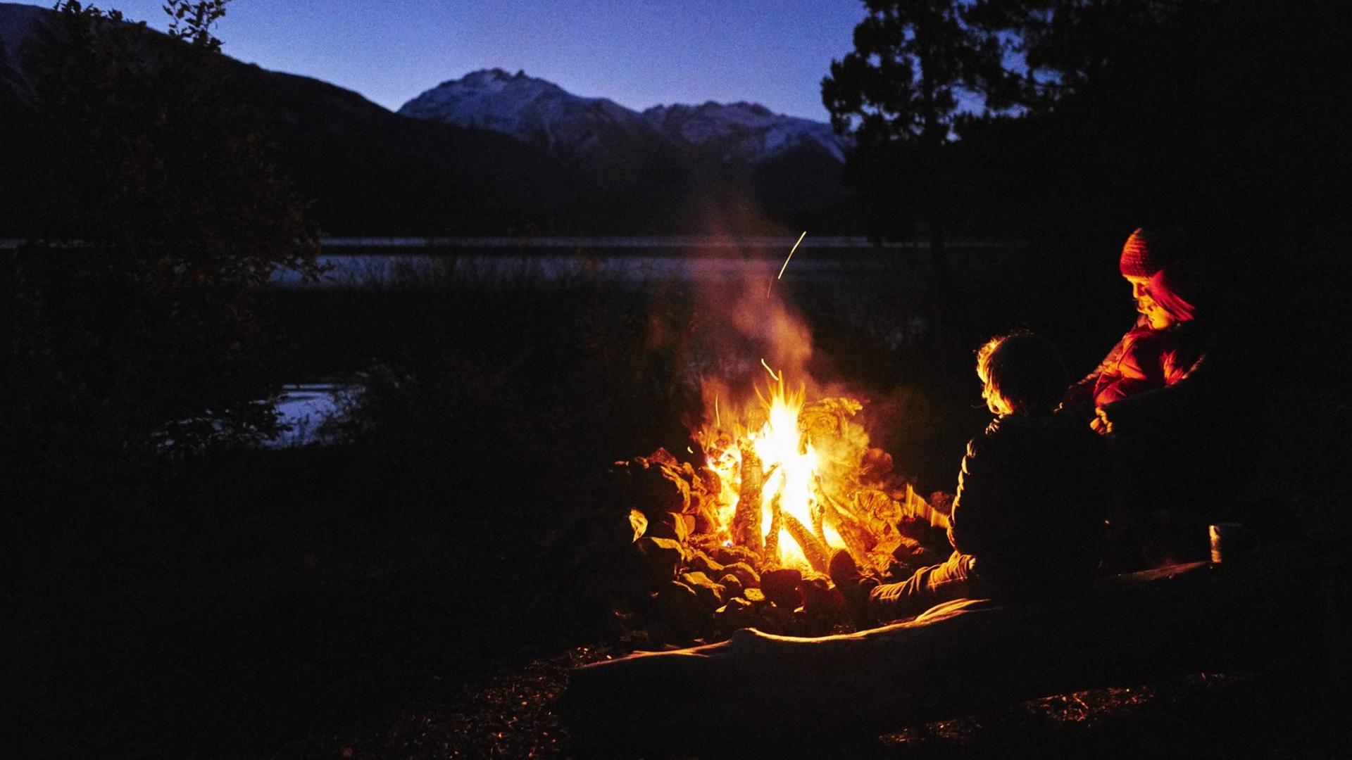 Menschen an einem Lagerfeuer in der Natur bei Nacht Menschen an einem Lagerfeuer in der Natur bei Nacht