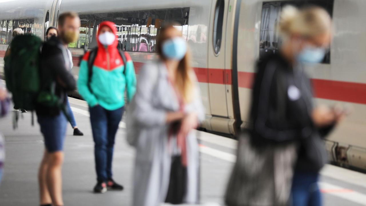 Reisende stehen auf dem Hauptbahnhof mit Masken an einem Zug. 