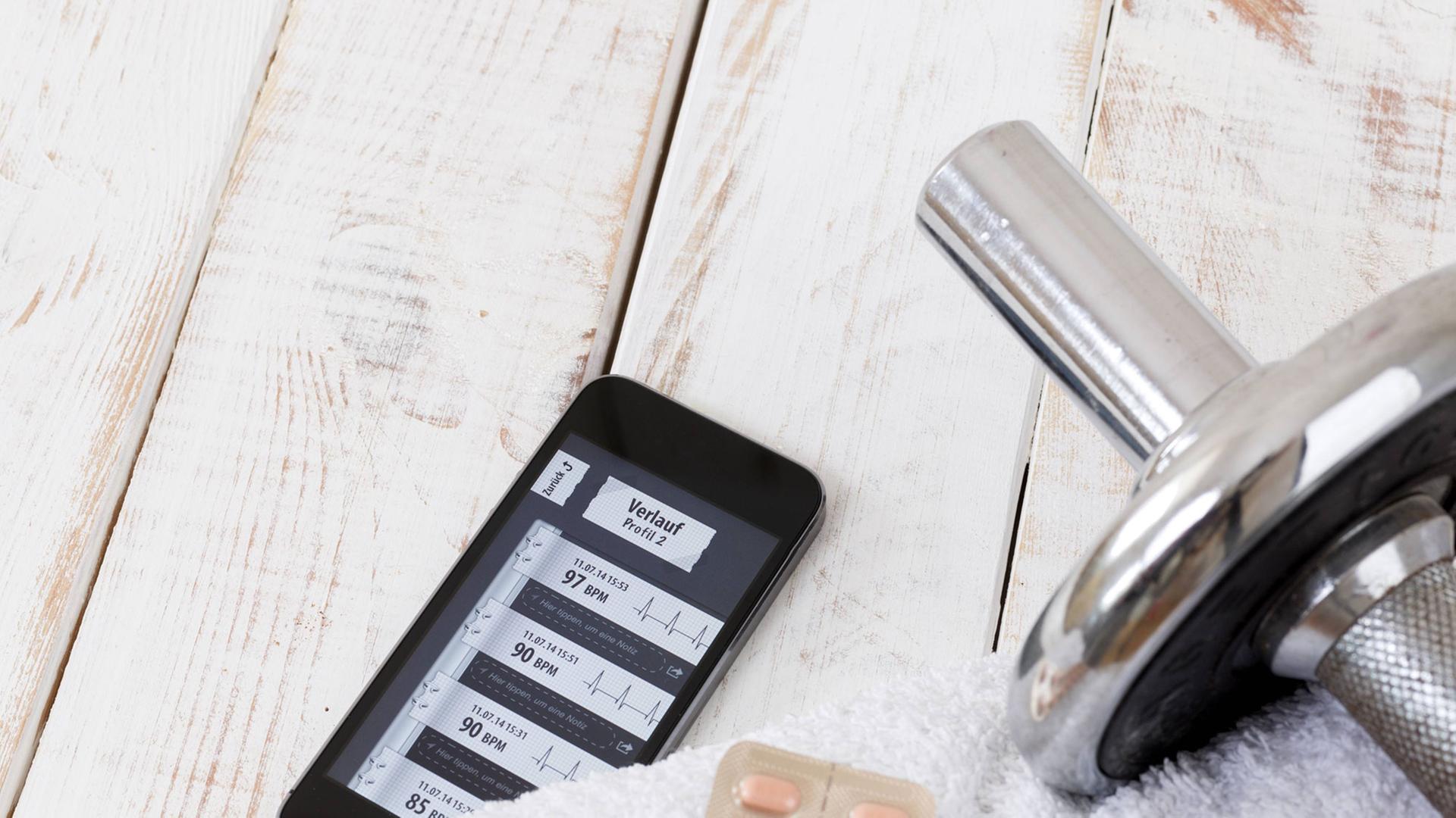 Smartphone mit einer Fitness-App, daneben eine Hantel auf einem Handtuch Smartphone mit einer Fitness-App, daneben eine Hantel auf einem Handtuch