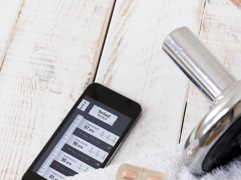 Smartphone mit einer Fitness-App, daneben eine Hantel auf einem Handtuch