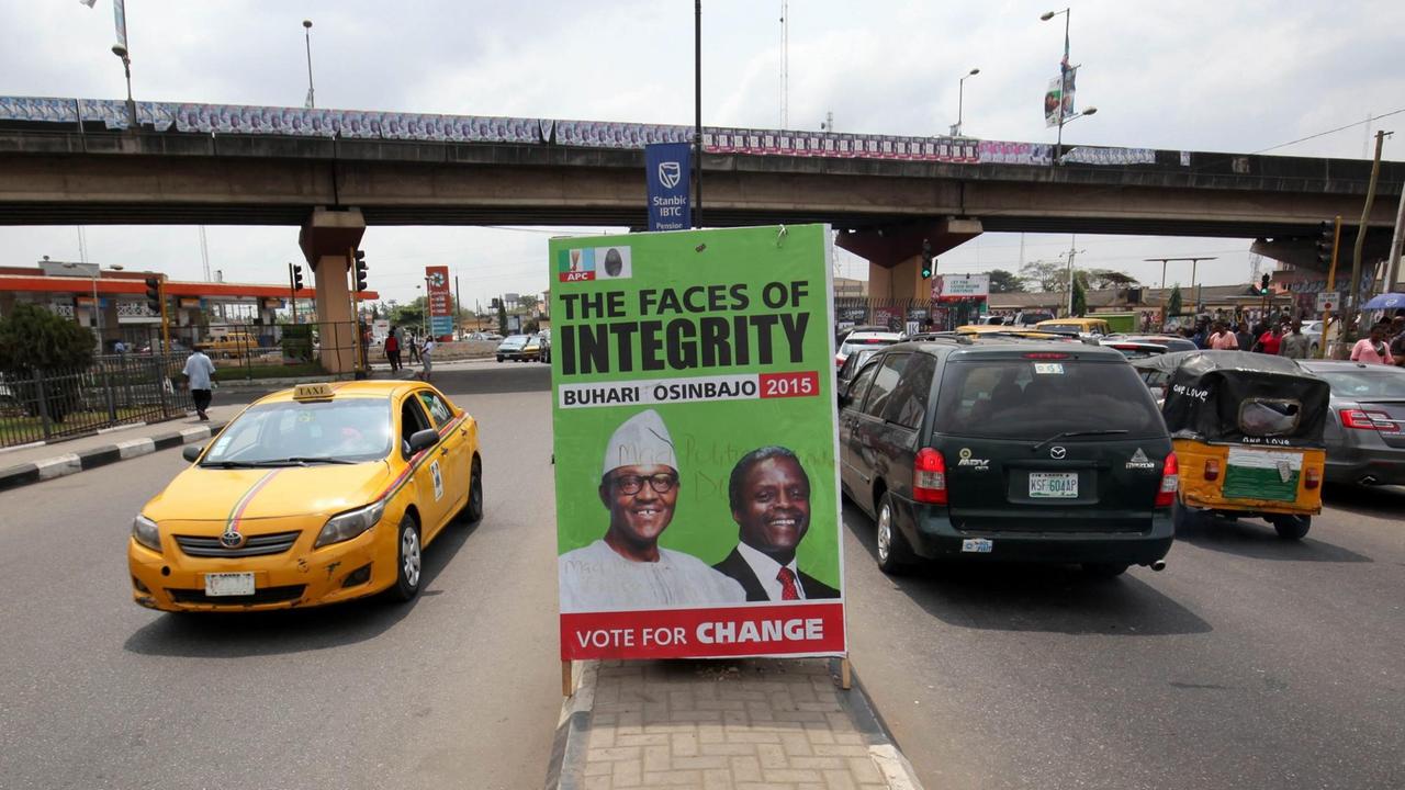 Autos fahren am 14.02.2015 an einem Wahlplakat  in Lagos, Nigeria vorbei. Das Plakat zeigt den Präsitentschaftskandidaten Muhammadu Buhari (L) und Vize-Kandidat Yemi Osinbajo (R).