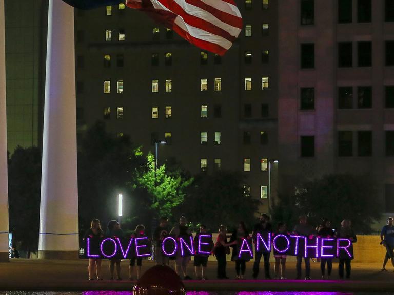 Menschen halten bei einer Nachtwache auf dem Platz vor der City Hall in Dallas LED-Lichter mit dem Schriftzug "Love one another" - liebt einander - hoch, aufgenommen am 11. Juli 2016.