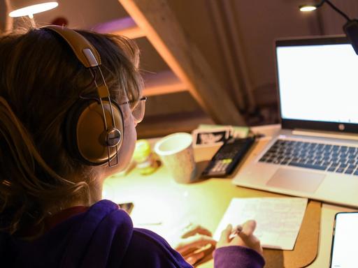 Ein Mädchen sitzt zu Hause an ihrem Schreibtisch und macht an ihrem Laptop Aufgaben für die Schule.