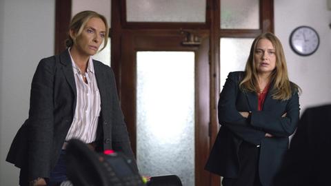 Die Schauspielerinnen Toni Collette, Merritt Wever stehen in einem Büro nebeneinander.