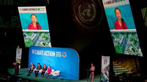 Bei einer Podiumsveranstaltung der Vereinten Nationen in New York sitzt die Aktivistin Greta Thunberg auf der Bühne. Sie wird auf zwei Bildschirme übertragen, die über der Bühne angebracht sind.