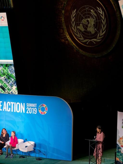 Bei einer Podiumsveranstaltung der Vereinten Nationen in New York sitzt die Aktivistin Greta Thunberg auf der Bühne. Sie wird auf zwei Bildschirme übertragen, die über der Bühne angebracht sind.