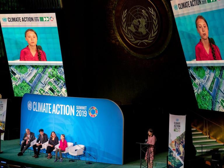 Bei einer Podiumsveranstaltung der Vereinten Nationen in New York sitzt die Aktivistin Greta Thunberg auf der Bühne. Sie wird auf zwei Bildschirme übertragen, die über der Bühne angebracht sind.