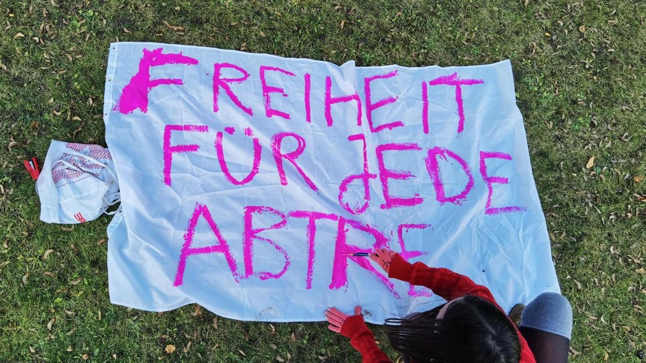 Eine junge Frau bemalt ein Transparent auf dem "Freiheit für jede Antreibung" in pinker Farbe zu lesen ist. Eine junge Frau bemalt ein Transparent auf dem "Freiheit für jede Antreibung" in pinker Farbe zu lesen ist.