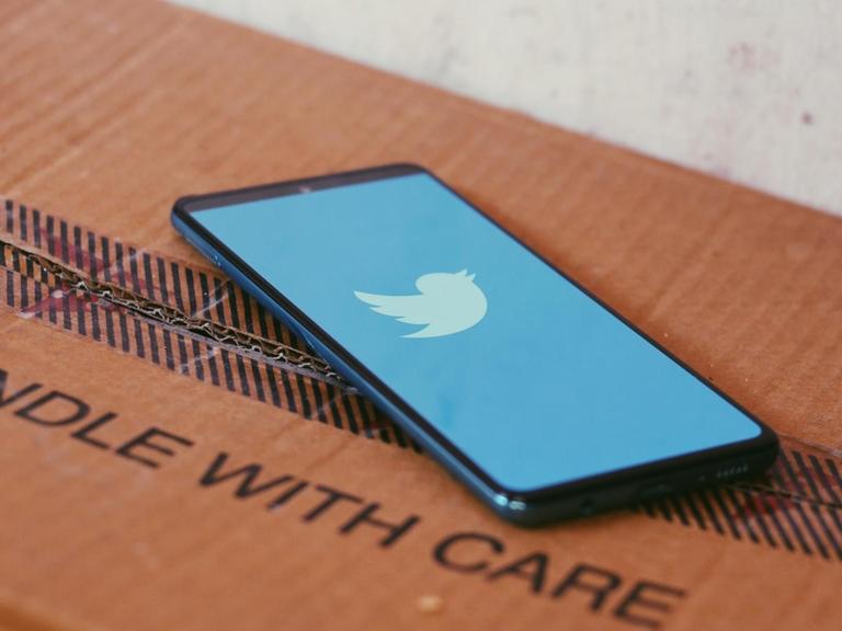 Auf einem Smartphone, das auf einem Karton liegt, ist das Twitter-Logo zu sehen.