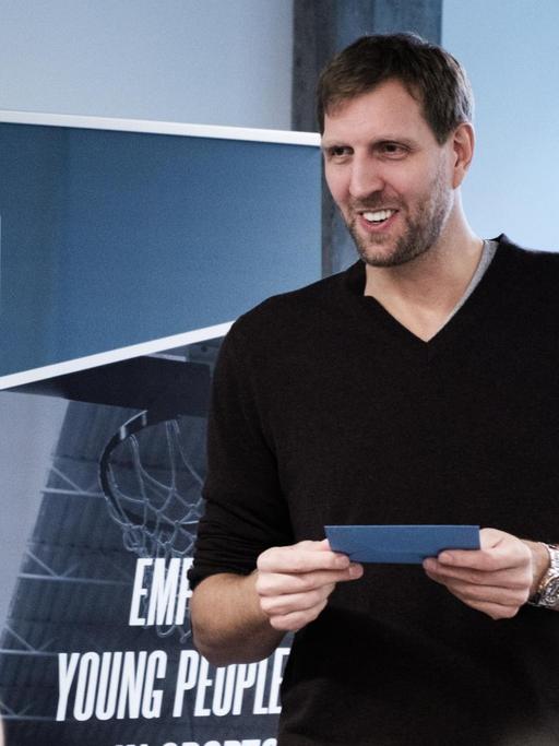 Jugendliche stehen im Halbkreis um Dirk Nowitzki, die eine blaue Moderationskarte in seinen Händen hält.
