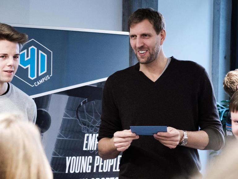 Jugendliche stehen im Halbkreis um Dirk Nowitzki, die eine blaue Moderationskarte in seinen Händen hält.