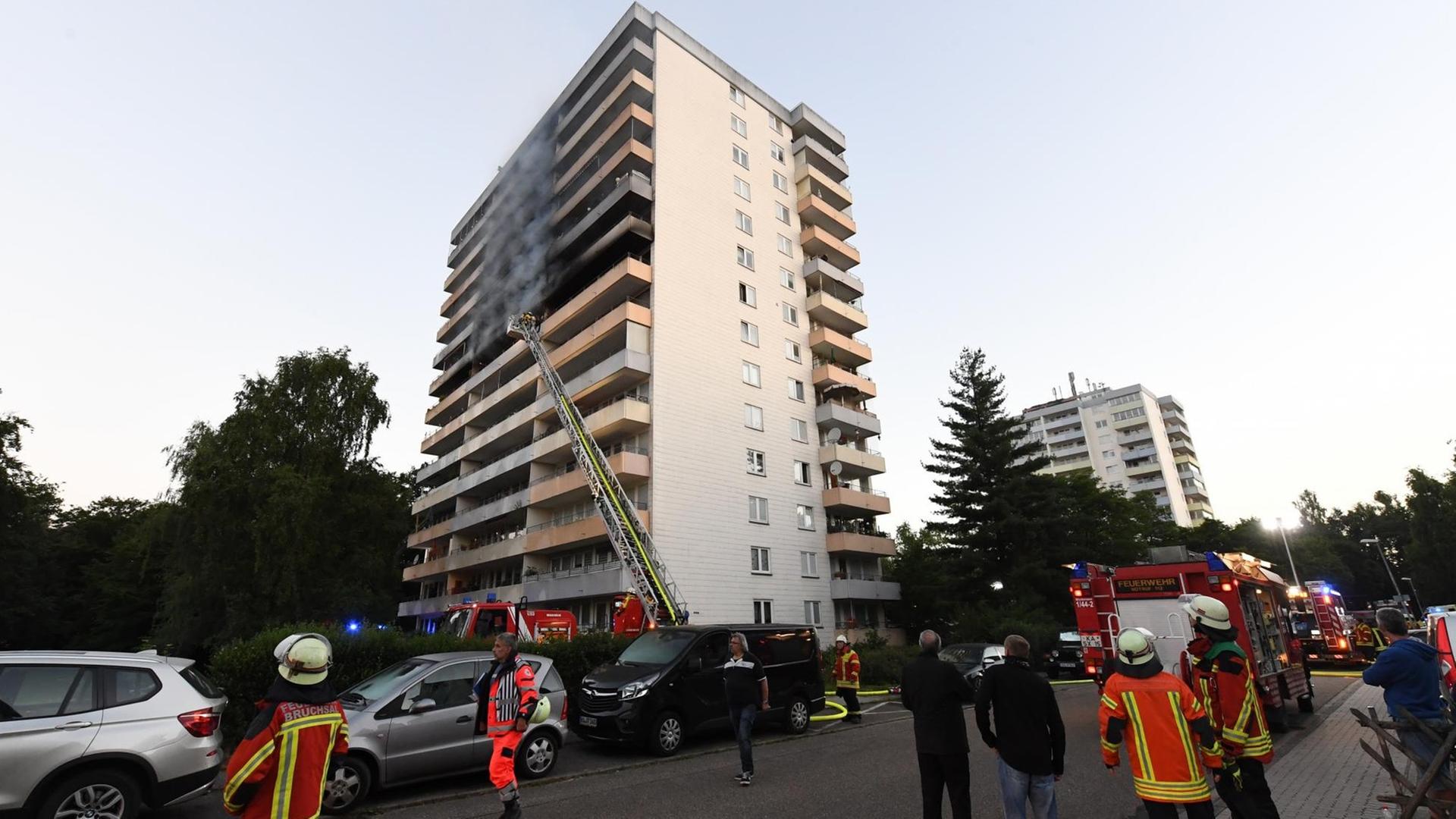 Feuerwehrleute stehen vor einem Hochhaus in Stutensee bei Karlsruhe. Das Feuer war in einer Wohnung im siebten Obergeschoss des 13-stöckigen Mehrfamilienhauses ausgebrochen.