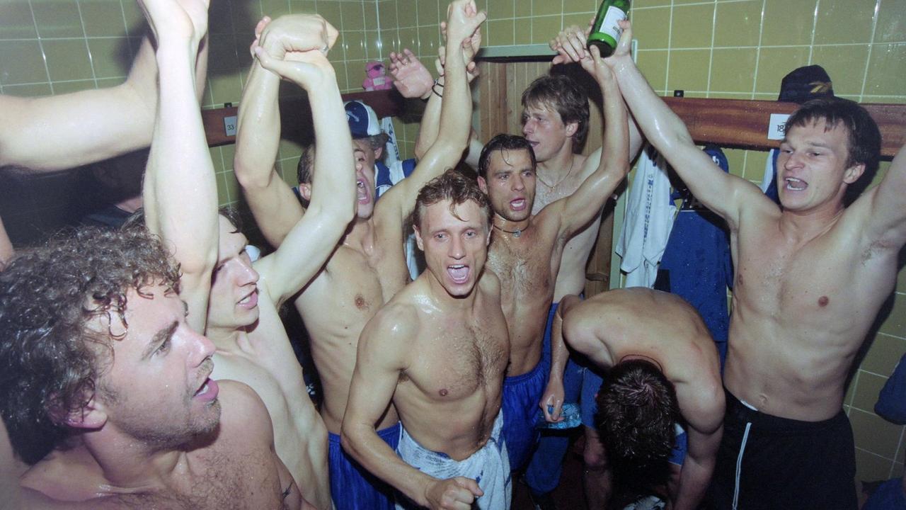 Fußballspieler feiern mit nacktem Oberkörper ausgelassen in einem großen Duschraum