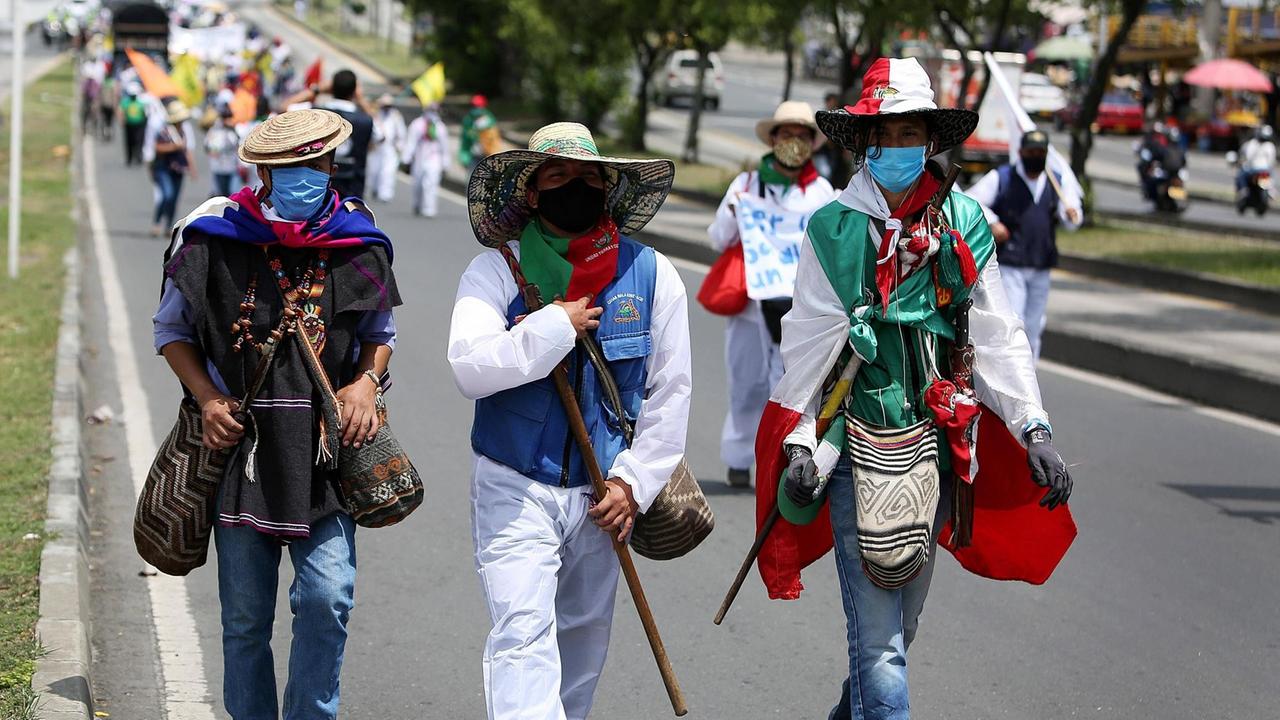 Demonstranten in traditioneller bunter Kleidung der Indigenen laufen auf einer Straße in Cali. Demonstranten in traditioneller bunter Kleidung der Indigenen laufen auf einer Straße in Cali.