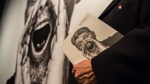 Ein Mann hält im Auktionshaus Sotheby's in London eine Broschüre über die private Kunstsammlung des verstorbenen Musikers David Bowie in der Hand.