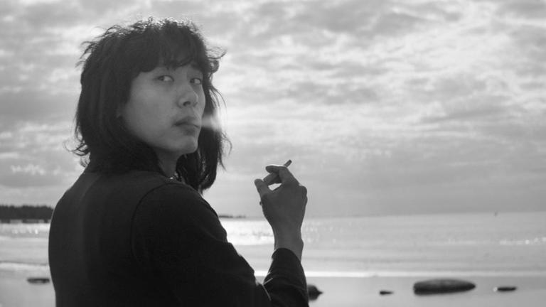Schwarzaufnahme eines asiatischen Schauspielers, der Zigarette rauchend am Strand steht und nachdenklich über seine Schulter blickt. Schwarzaufnahme eines asiatischen Schauspielers, der Zigarette rauchend am Strand steht und nachdenklich über seine Schulter blickt.