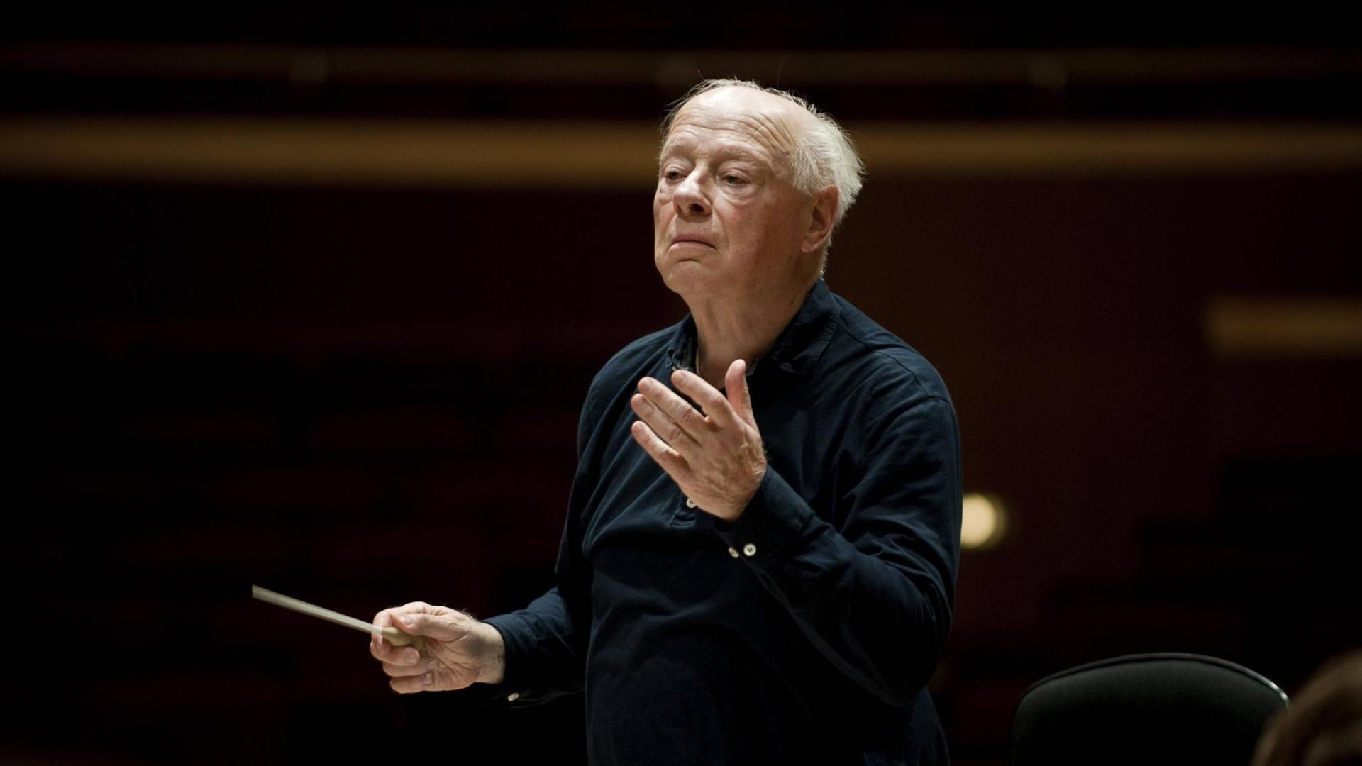 Der Dirigent Bernard Haitink steht auf einer dunklen Bühne und dirigiert ein nicht sichtbares Symphonie Orchester. Der Dirigent Bernard Haitink steht auf einer dunklen Bühne und dirigiert ein nicht sichtbares Symphonie Orchester.