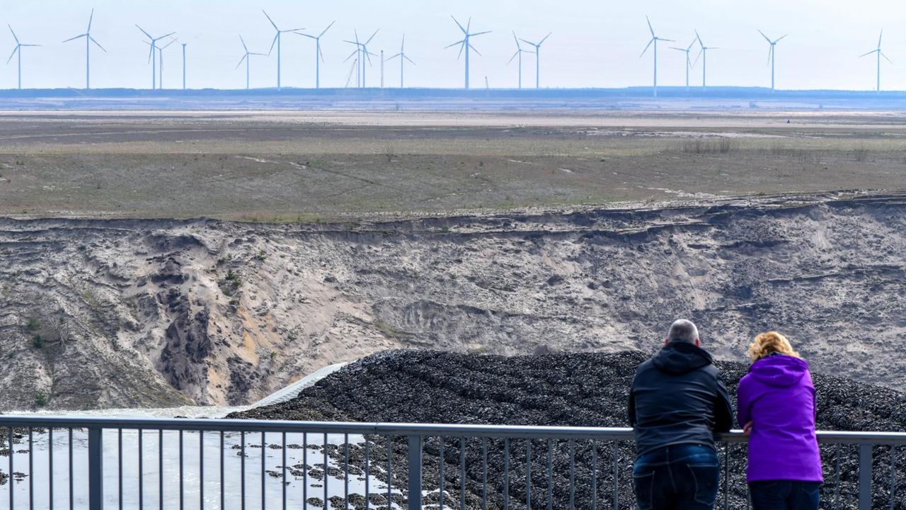 Besucher stehen am Einlaufbauwerk am ehemaligen Braunkohletagebau Cottbus-Nord. Die gesamte Landmasse bis zu den Windrädern im Hintergrund soll später einmal von Wasser bedeckt sein. Besucher stehen am Einlaufbauwerk am ehemaligen Braunkohletagebau Cottbus-Nord. Die gesamte Landmasse bis zu den Windrädern im Hintergrund soll später einmal von Wasser bedeckt sein.